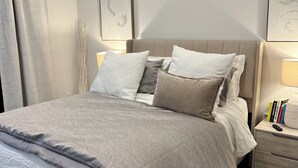 A neatly made bed with a grey and white duvet, a fluffy white rug, and a bedside table with books and a remote control. - Ultra Chic 1-bedroom apartment with AC, fitness room in cool Austin (Austin)