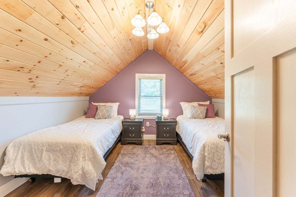 A bedroom with two beds, a wooden ceiling, a window, and a door.