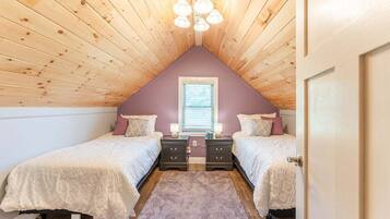 A bedroom with two beds, a wooden ceiling, a window, and a door.