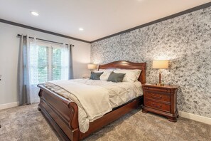 Une chambre à coucher avec un lit en bois, deux tables de chevet, une fenêtre avec des rideaux et un mur à motifs.