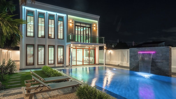 Una casa moderna de dos pisos con piscina, balcón y una cascada.