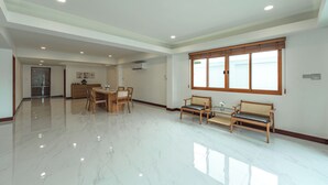 Una habitación amplia con piso de mármol pulido, un área de comedor con muebles de madera y ventanas grandes con marcos de madera.