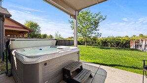 Un jacuzzi en un área exterior cubierta con un escalón para acceder, rodeado de un césped cuidado y una valla de madera.