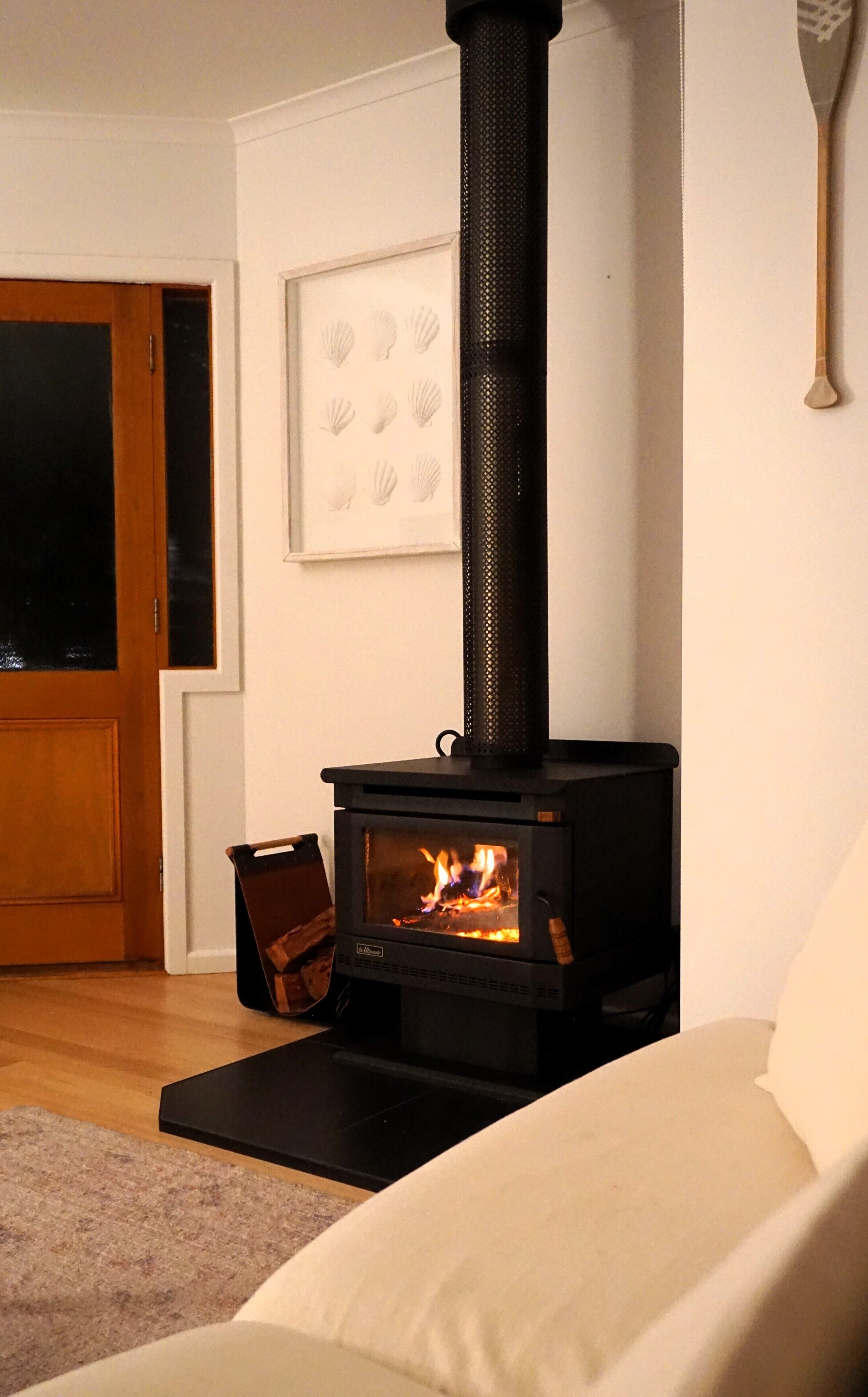 A room with a black wood-burning stove, a white sofa, and a framed picture on the wall.