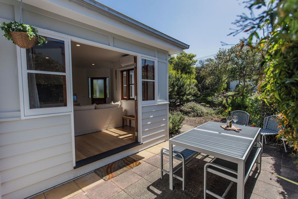 A modern house with a patio area featuring a table and chairs, a hanging plant, and a cozy seating area inside.