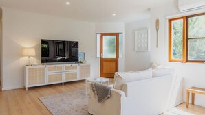 A modern living room with a white sofa, a flat-screen TV, a white cabinet, and a wooden door. - Chic Beachside Stay – Near River, Shops & Cafés (Ocean Grove)