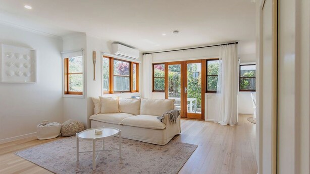A spacious living room with a white sofa, a coffee table, and a large window with curtains. - Chic Beachside Stay – Near River, Shops & Cafés (Ocean Grove)
