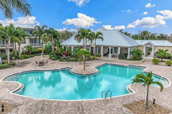 A swimming pool with a curved design, surrounded by palm trees and a building with a light blue roof.