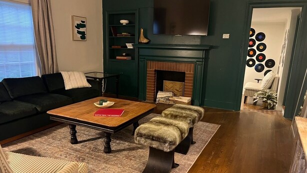 A living room with a dark green wall, a fireplace, a television, and a coffee table. - Village District - Historic 2-bedroom house in Raleigh (Raleigh)