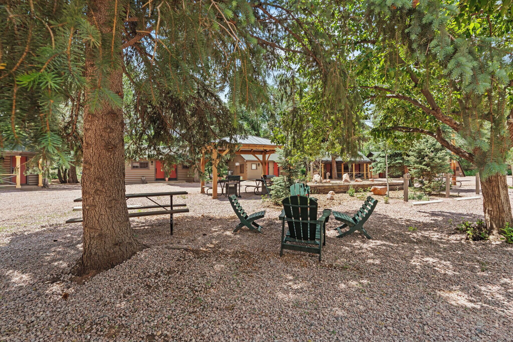 Et hyggeligt udendørs opholdsområde med Adirondack-stole, et picnicbord og en træpavillon.