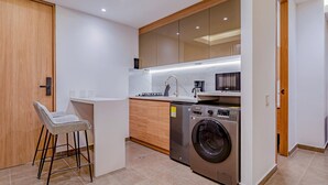 Une cuisine compacte équipée d’un lave-linge intégré, d’une machine à café et d’un tabouret de bar.