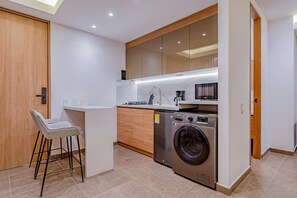 A compact kitchen with a built-in washing machine, a coffee maker, and a bar stool. - Edificio Urus (Cali)