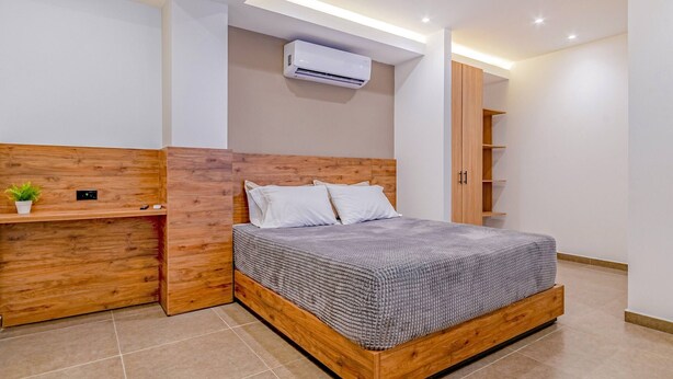 Une chambre moderne avec un cadre de lit en bois, une table de chevet, une étagère intégrée et un climatiseur fixé au mur.