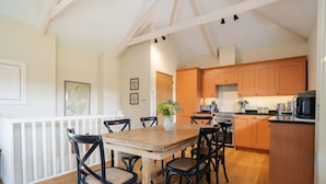 A dining area with a wooden table and chairs, a white railing, and a kitchen with wooden cabinets and appliances. - Cowlands 3 bed, barn conversion, pet friendly, three bedrooms, Sleeps 6 (Truro)