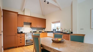 A kitchen with wooden cabinets, a large island with chairs, and a window with natural light. - Cowlands 3 bed, barn conversion, pet friendly, three bedrooms, Sleeps 6 (Truro)