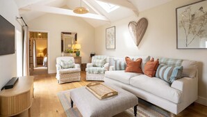 Ein geräumiges Wohnzimmer mit hohen Decken, einem weißen Sofa, gemusterten Sesseln und einer herzförmigen Wanddekoration.