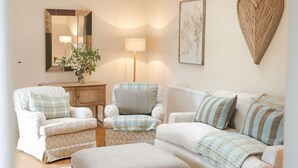 Ein gemütliches Wohnzimmer mit zwei Sesseln, einem Sofa, einem Beistelltisch mit Lampe, einem Spiegel und einer herzförmigen Wanddekoration.