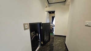 Un pasillo con lavandería, un electrodoméstico negro y suelo de baldosas.