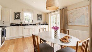 A modern kitchen with white cabinetry, a large dining table, and a hanging light fixture.