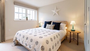 A bedroom with a large bed, two bedside tables with lamps, a star decoration on the wall, a window with curtains, and a potted plant on the windowsill.