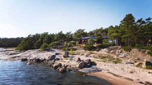 Une propriété située sur la côte, avec un rivage rocheux, une petite plage et un ensemble de cabanes entourées d’arbres.