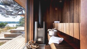 Une terrasse en bois dotée d’un poêle à bois intégré, une fenêtre donnant sur un lac et un banc avec une serviette.