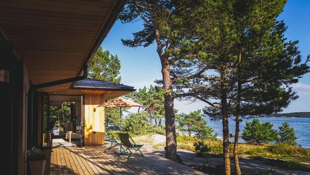 Une terrasse en bois avec des sièges extérieurs, un espace abrité et une vue sur un lac et des arbres.