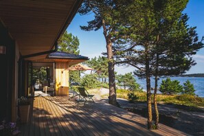 A wooden deck with outdoor seating, a covered area, and a view of a lake and trees. - Stay North - Svärdskog (Hanko)