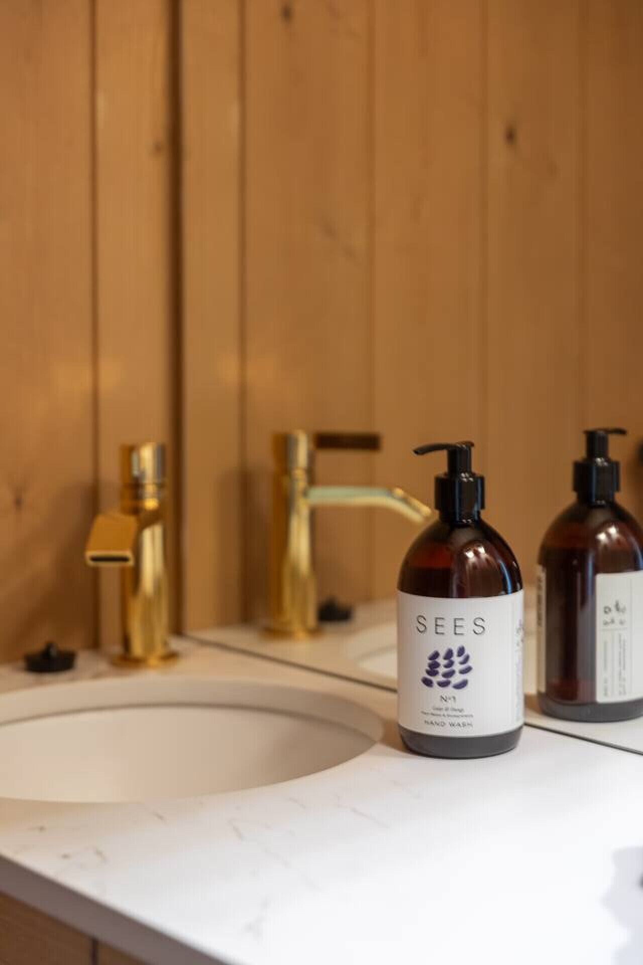 Un baño con un lavamanos blanco, dos botellas de jabón de manos y un grifo dorado.