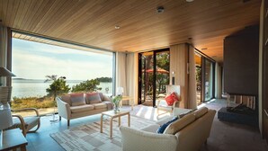 Un salon moderne doté d’une grande fenêtre donnant sur un plan d’eau, d’une cheminée et d’un coin salon confortable.