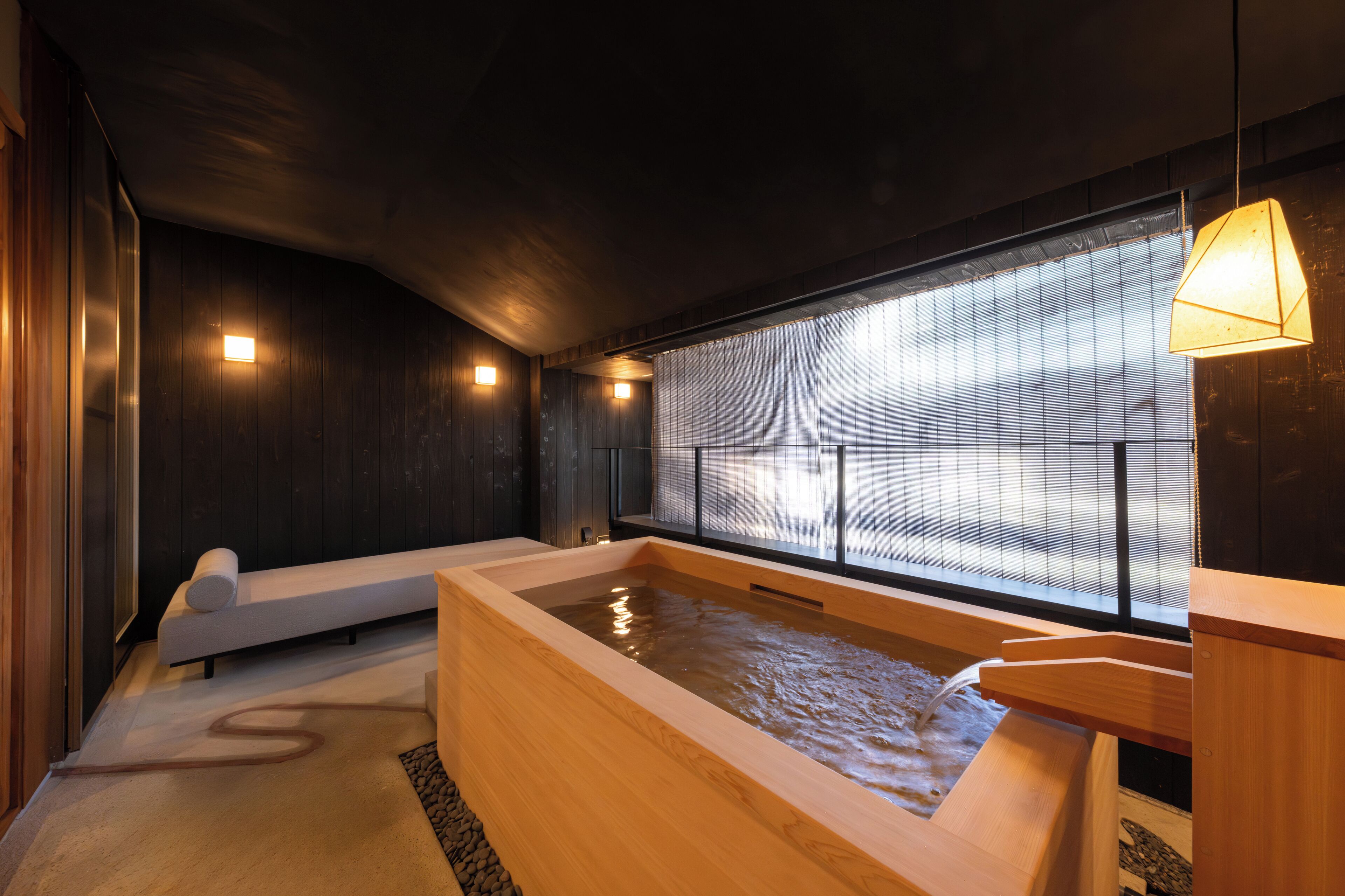 A traditional Japanese onsen with a wooden bathtub, a seating area, and a view through a shoji screen.