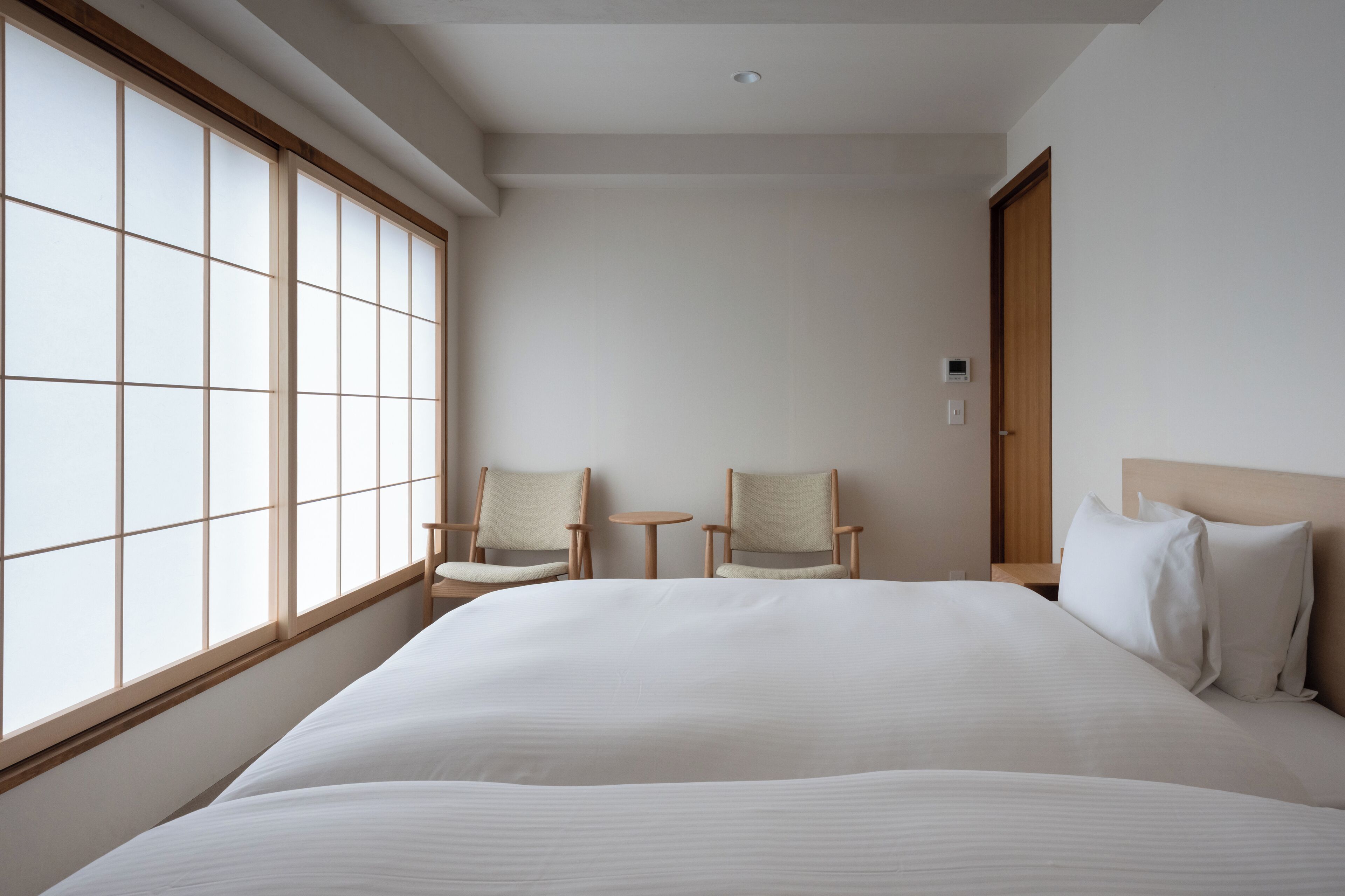 A hotel room with a large bed, two chairs, a small table, and a sliding door.
