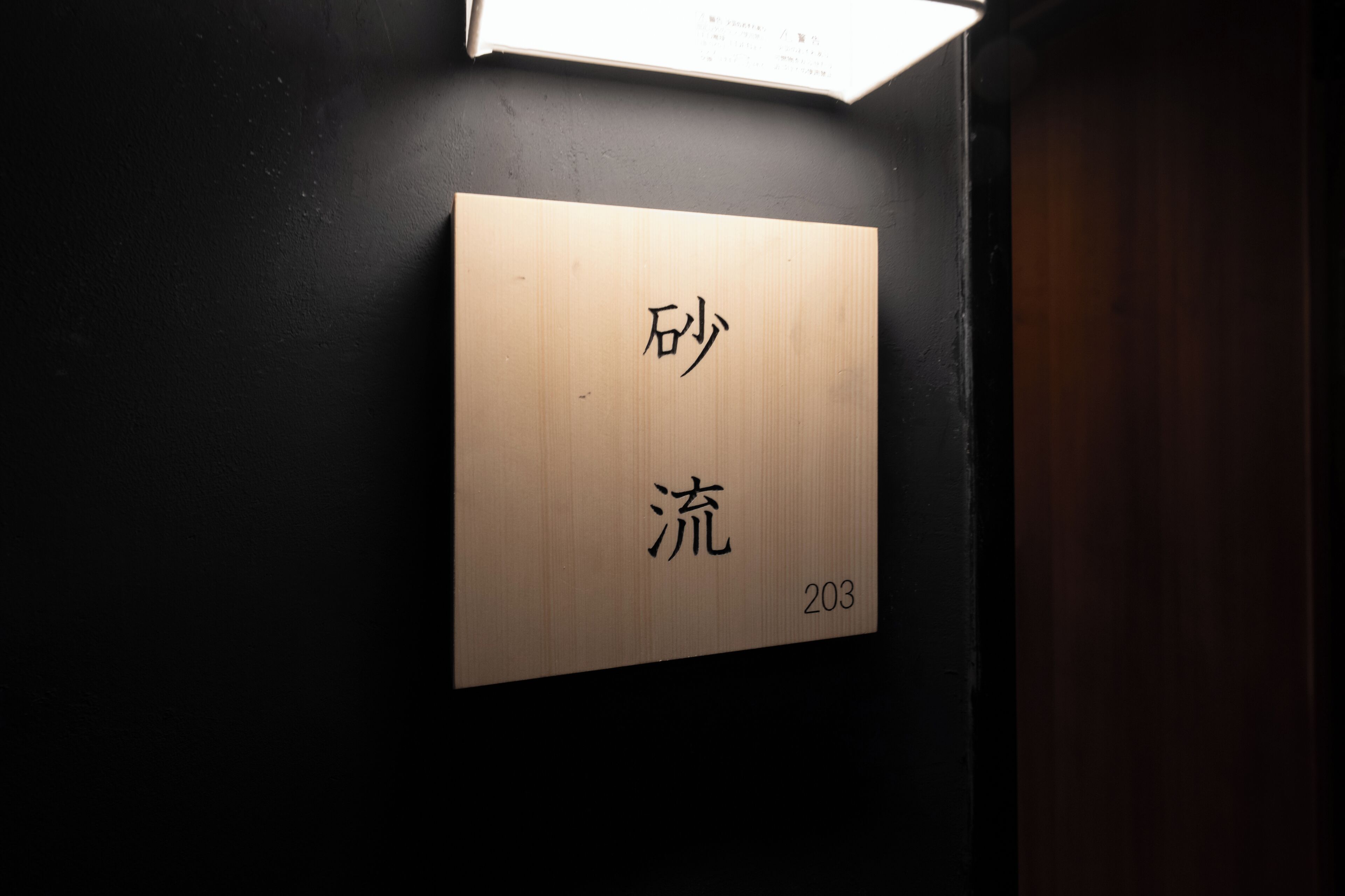 Ein hölzernes Schild mit chinesischen Schriftzeichen und der Nummer 203.