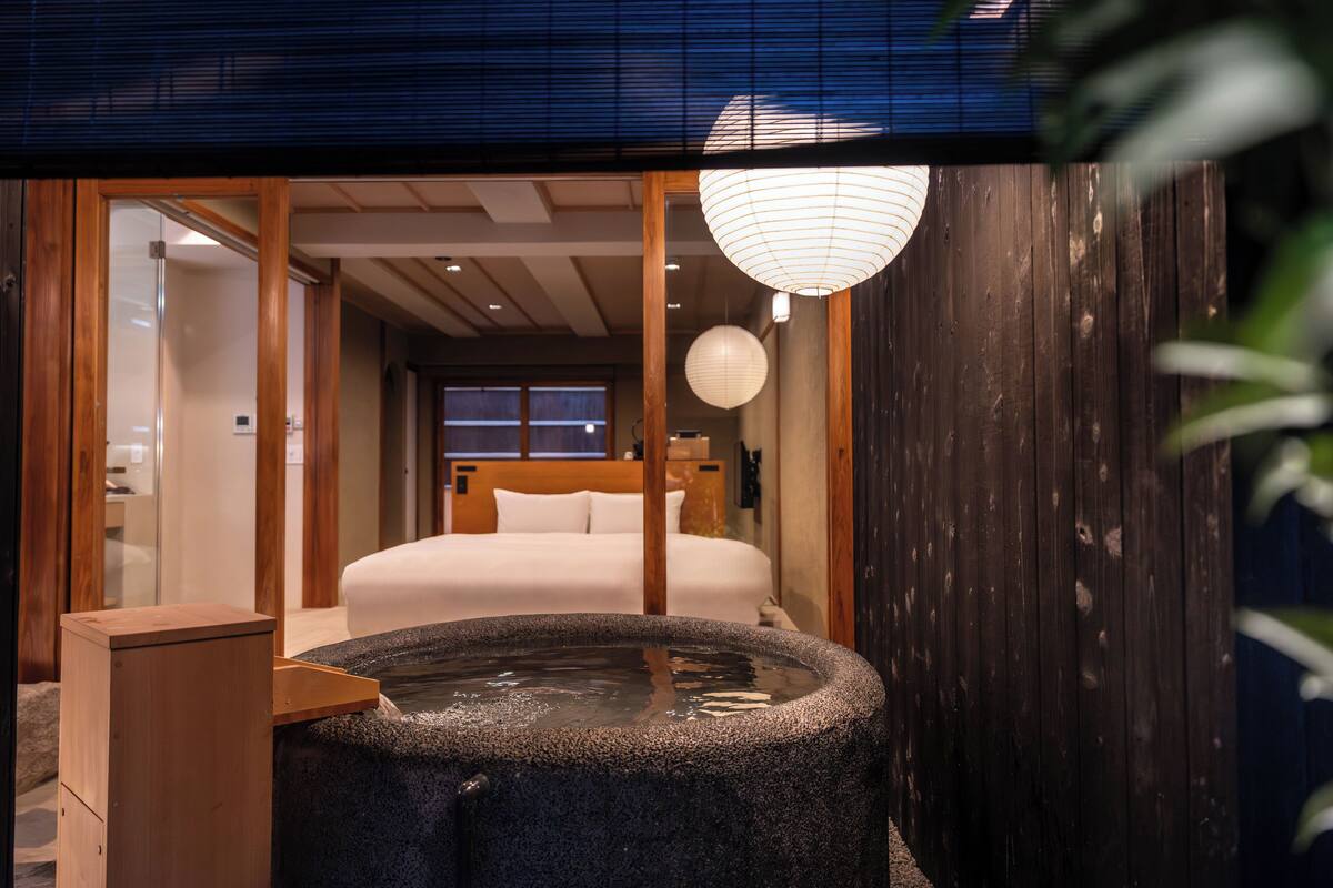 Ein traditioneller japanischer Raum mit Bett, Holzboden, Steinbad und Holzwand.