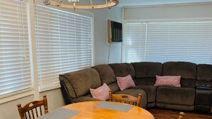 A dining area with a wooden table and chairs, a brown sofa with cushions, and a chandelier.