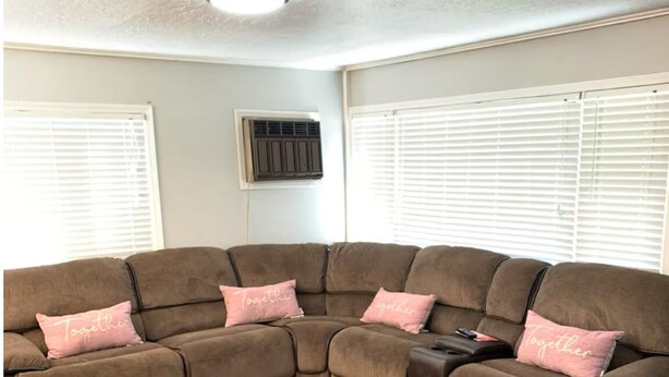A sectional sofa with pink pillows in a room with wooden flooring and white walls.