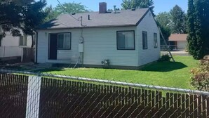 A single-story house with a gabled roof, a chimney, and a fenced backyard.
