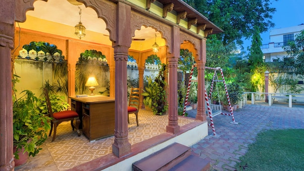 A covered outdoor seating area with wooden chairs and tables, surrounded by potted plants and a patterned floor. - Ikshana Boutique (Jaipur)