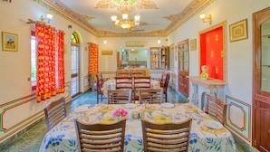 A dining area with a chandelier, red curtains, and a table set for four. - Ikshana Boutique (Jaipur)