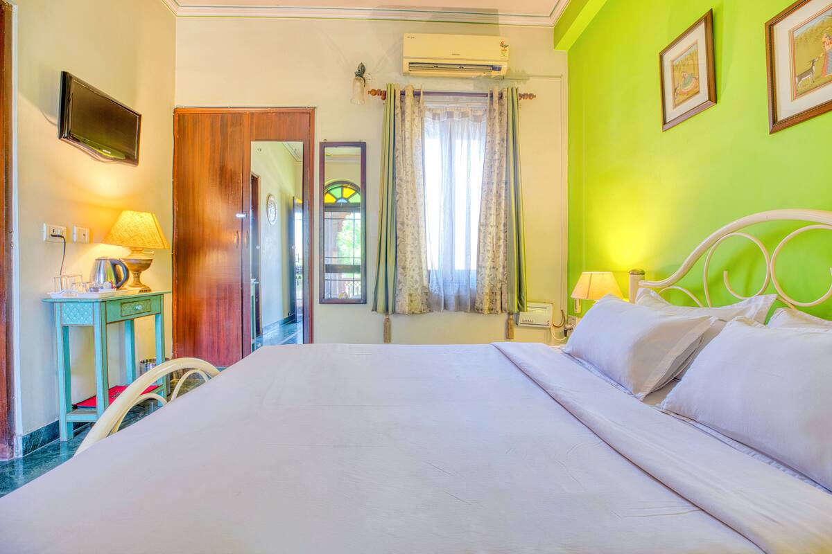 Une chambre d’hôtel avec un grand lit, un bureau avec une lampe, une chaise, une télévision et une fenêtre avec des rideaux.