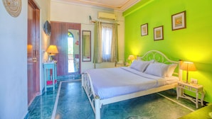A room with a bed, two bedside tables with lamps, a ceiling fan, and a door with a mirror. - Ikshana Boutique (Jaipur)