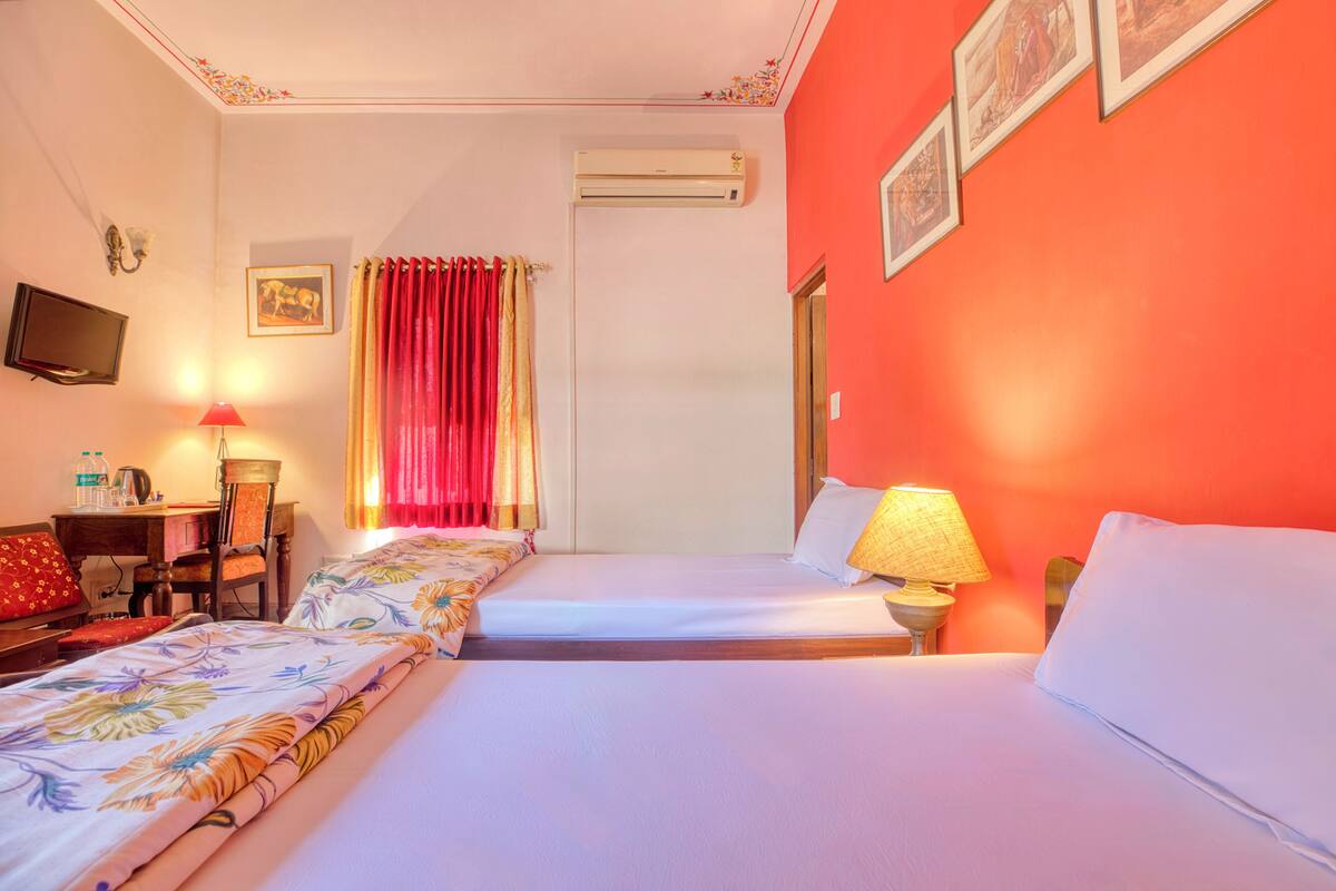 Une chambre d’hôtel avec deux lits, un bureau avec une chaise, une télévision et un appareil de climatisation.
