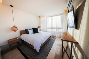 A modern bedroom with a large bed, bedside tables, a desk, and a TV. - Distrito Puerto – Ocean & Mangrove Views (Puerto Morelos)