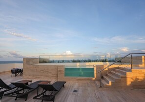 A rooftop terrace with a glass-enclosed infinity pool, lounge chairs, and a staircase leading to an upper level. - Distrito Puerto – Ocean & Mangrove Views (Puerto Morelos)