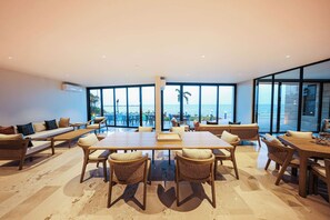 A spacious room with a large dining table, comfortable seating, and large windows offering a view of the sea. - Distrito Puerto – Ocean & Mangrove Views (Puerto Morelos)