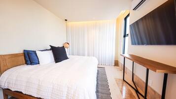 Une chambre à coucher avec un lit, une table de chevet, une télévision et une fenêtre avec des rideaux.