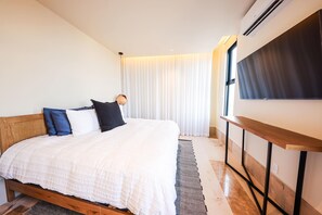 A bedroom with a bed, a bedside table, a TV, and a window with curtains. - Distrito Puerto – Ocean & Mangrove Views (Puerto Morelos)