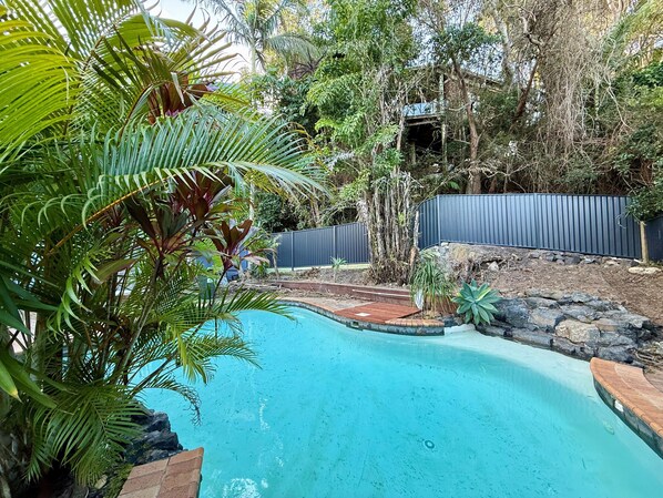 A swimming pool surrounded by lush greenery and a wooden deck. - Korora Court by Charlesworth (Coffs Harbour)