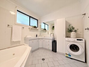 A modern bathroom with a bathtub, a built-in washing machine, and a window providing natural light.