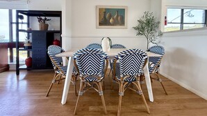 Un comedor con una mesa de madera y seis sillas con tapicería estampada. Hay un cuadro en la pared y una planta en maceta al lado.